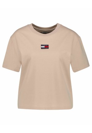 Beżowy krótki top Tommy Jeans z krótkim rękawem, okrągłym dekoltem i małą prostokątną naszywką z logo na środku klatki piersiowej.