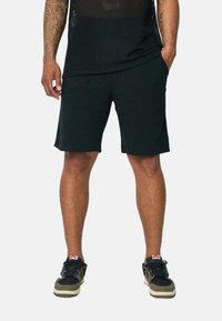 T-shirt de sport en mesh noir, shorts noirs et baskets noires avec des accents beiges ; axé sur le confort et la respirabilité pour les vêtements de sport.