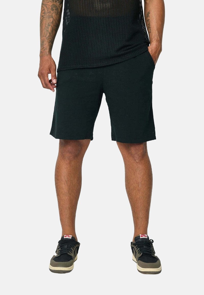 T-shirt de sport en mesh noir, shorts noirs et baskets noires avec des accents beiges ; axé sur le confort et la respirabilité pour les vêtements de sport.