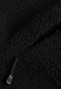 Zwarte fleece stof met een gestructureerd oppervlak, voorzien van een ritssluiting en een kleine trek lus. De stof is zacht en dicht.