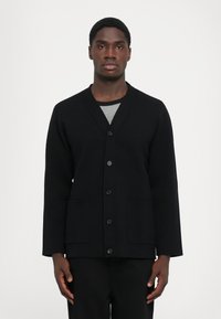 Crna cardigan jakna s V izrezom, prednjim gumbima i dva uložena džepa. Izrađena od teksturirane tkanine, s dugim rukavima.