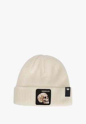 Cream knit beanie with ribbed texture, featuring a black patch displaying a skull and the word "CANCELLED." Cuffed design.