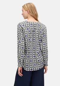 Langärmlige Bluse aus leichtem Stoff, mit einem geometrischen Muster in Blau, Grün und Weiß, einem abgerundeten Saum und einem gerafften Rückendetail.