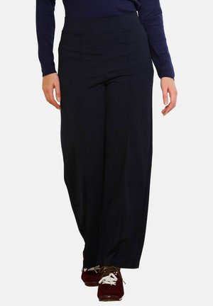 Sügavsinised laia lõikega püksid, millel on sile kangas, kõrge vöökoht ja voldi disain; koos pruuni spordijalanõude ja sobiva tumeda toppiga.