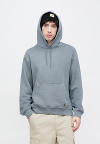 Szara bawełniana bluza z kapturem, przednią kieszenią kangura, sznurkiem do regulacji kaptura oraz naszywką z logo na dolnej części przodu. Stylizowana z beżowymi szortami cargo.