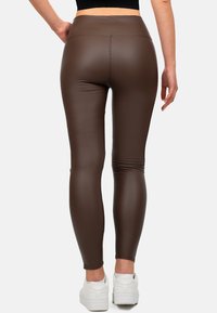 Leggings in finta pelle marrone con vita alta, texture liscia e vestibilità aderente. Abbinati a sneakers bianche per un contrasto.