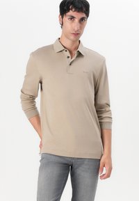 Beige long-sleeve polo shirt with a three-button placket and subtle logo. Made of soft material, features ribbed cuffs and a relaxed fit.