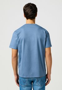 Blauwe katoenen t-shirt met een ronde hals en korte mouwen, met een gladde textuur. Draagt door een persoon die van zich af kijkt, gecombineerd met lichte denim.