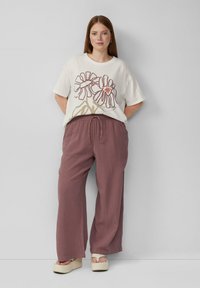 Overmaatse crèmekleurige T-shirt met bloemenprint, gecombineerd met losse, textuurvolle mauve broek. Platform schoenen maken de outfit compleet.