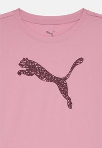 Pink short-sleeve t-shirt featuring a dark purple leaping cat logo. The fabric has a smooth, textured finish with a crew neckline.