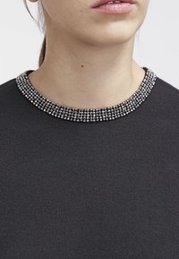 Zwarte trui met een gestructureerde kraag voorzien van metalen versieringen. Nauwsluitende pasvorm met een gladde stofoppervlakte, met een gedetailleerde halslijn.