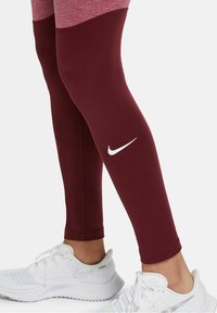 Vinsvarta leggings med en slät yta och hög midja. Har en vit Nike-logotyp och är matchade med vita sportskor.