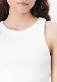 White ribbed tank top with a round neckline and wide shoulder straps, featuring a smooth texture that enhances the fitted design.