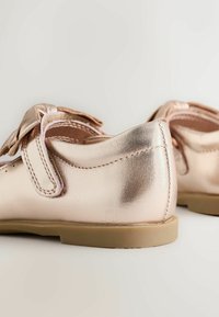 Metalen rosegouden schoenen met een gladde textuur, een ronde neus en een verstelbare klittenbandsluiting. De zolen zijn van rubber met een lichtbruine tint.