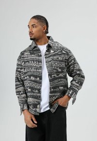 Grijs-wit geruit flanellen overhemd met kraag, knoopsluiting aan de voorkant en een losse pasvorm, gecombineerd met een witte T-shirt eronder.