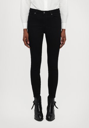 Black skinny jeans made of denim, featuring a classic five-pocket design, metal button closure, and stitching details. Worn with black ankle boots.