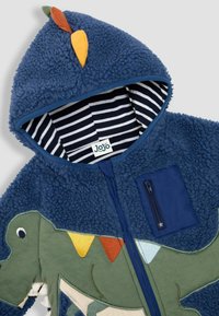 Jachetă din fleece cu glugă de culoare bleumarin, cu aplicație de dinozaur. Prezintă o căptușeală interioară în dungi, buzunar cu fermoar și accente din țesătură colorată.