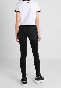 Svarta slim-fit jeans med definierad midja och bakfickor, ihop med en vit beskuren t-shirt med svart krage och logga. Svarta sneakers.