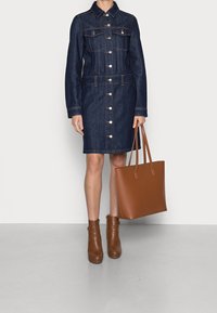 Denim dress with long sleeves, button front, and two chest pockets. Paired with a brown tote bag and brown ankle boots.