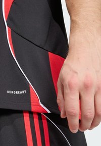 T-shirt de sport noir avec accents rouges, arborant un design texturé, un passepoil blanc et le logo "AEROREADY" près de l'ourlet.