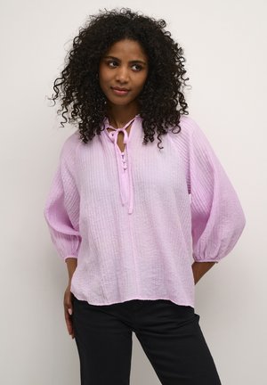 Helles rosa, zerknittertes Blusenshirt mit einer Krawattenknopfverschluss und Knopfdetails. Mit Puffärmeln und lockerer Passform. Getragen mit schwarzen Hosen.