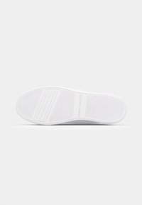 Sola de ténis brancos com padrão de aderência texturizado, linhas horizontais e nome da marca visível. Forma plana, material suave, design minimalista.