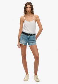 Witte tanktop, lichtblauwe denim shorts met een rafelige zoom, zwarte riem, beige sneakers. Eenvoudig ontwerp, casual pasvorm, minimale details.