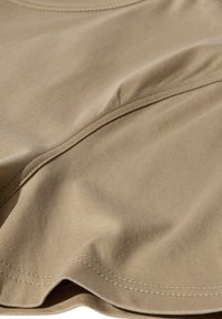Beige bomuldsstof med glat tekstur, der har syninger langs kanterne og en let fald, der fremviser bløde folder og blide kurver.