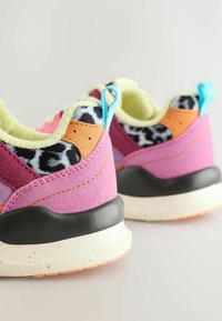 Baskets colorées avec un mélange de suède rose et violet, une semelle noire texturée, et un accent à motif tacheté sur le talon. Doublure vert clair.