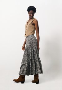 Linnen vest in tan met knopen, gecombineerd met een zwart-wit bloemenprint maxi-rok en bruine heeled cowboylaarzen.