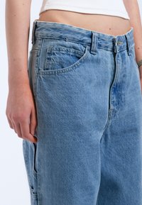 Light blue denim jeans with a relaxed fit, five pockets, visible stitching, and a slight wash effect on the fabric texture.