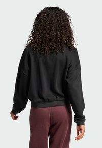 Sudadera negra corta con mangas largas, dobladillo acanalado y puños anchos, combinada con pantalones burdeos. Tejido suave y texturizado.