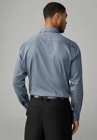 Camisa de manga larga azul claro con una textura suave, detalle de canesú trasero y puños abotonados, combinada con pantalones negros ajustados.
