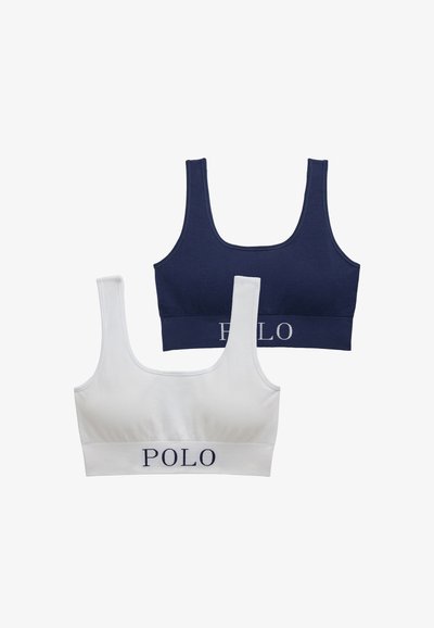 Dvě podprsenky bez kostice: jedna námořnicky modrá a jedna bílá. Žebrovaná textura se širokými ramínky a elastickými pásky s nápisem „POLO“ v kontrastních barvách.