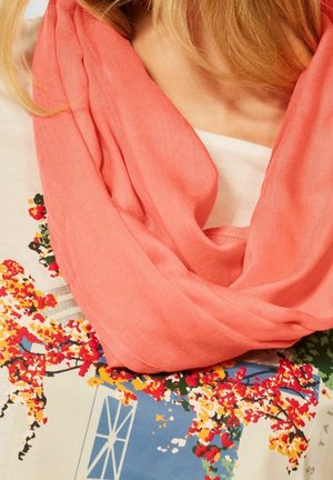 Écharpe corail en tissu léger, portée de manière décontractée, associée à une chemise à motifs floraux avec des accents colorés.