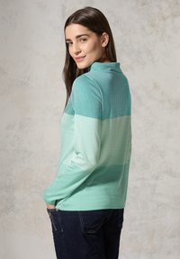 Turquoise gestreepte pullover met een hoge kraag, voorzien van een gradient ontwerp en lange mouwen, gecombineerd met donkere jeans. Soepele textuur.