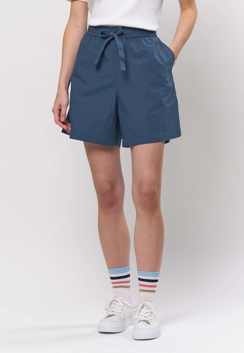 Dunkelblaue Shorts mit Kordelzug in der Taille, Seitentaschen, gerade geschnitten, kombiniert mit weißen Turnschuhen und mehrfarbigen, gestreiften Socken.