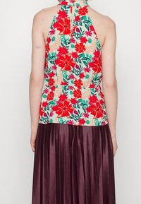 Květinový halter top v krémové barvě s červenými a zelenými květinami, spárovaný s vínovou plisovanou sukni. Top má výstřih ve tvaru klíčové dírky a přiléhavý pas.