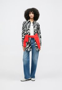 Μαύρο και άσπρο πουκάμισο με ρίγες ζέβρας, λευκό τοπ, μπλε τζιν με φουσκωτά μπατζάκια, κόκκινο μαντήλι δεμένο στη μέση και ανοιχτόχρωμα παπούτσια.