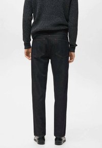 Jeans de mezclilla oscura con corte recto, con dos bolsillos traseros y costuras visibles. Llevados con un suéter negro texturizado y zapatos negros.