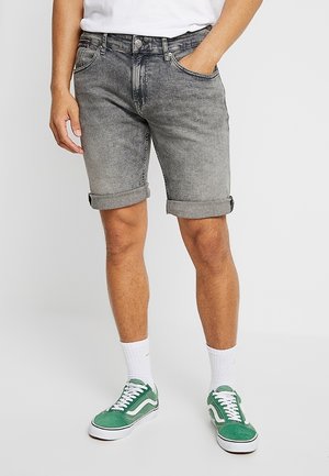 Shorts in denim grigio con risvolti, caratterizzati da una finitura sbiadita, design a cinque tasche e chiusura con bottone anteriore. Indossati con scarpe da ginnastica verdi.