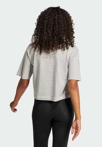 Grå, kortärmad t-shirt med mjukt material, kombinerad med svarta leggings. Bakifrån visar den en avslappnad, lös passform.