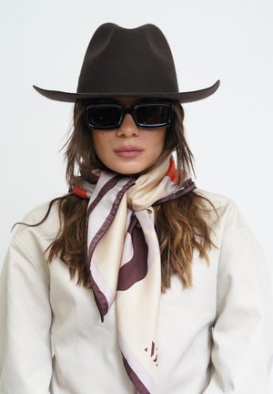 Brown wide-brim hat, black square sunglasses, and a patterned silk scarf in beige, brown, and red tones, paired with a light-colored jacket.