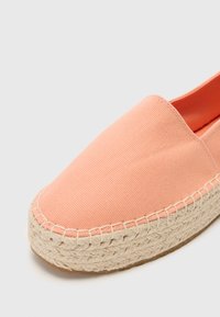 Espadrille en toile orange pâle avec un bout arrondi, semelle en corde de jute et couture contrastante le long du bord. Design simple et facile à enfiler.