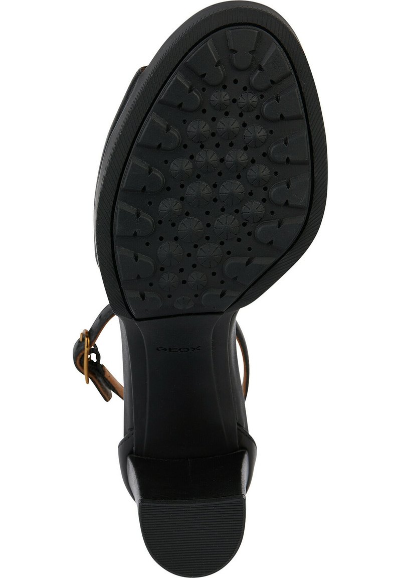 Sandal nera con suola in gomma testurizzata, caratterizzata da un tacco basso e una fibbia dorata su una cinghia in pelle. Sono visibili dei fori di ventilazione.