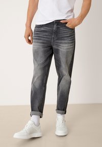 Graue Denim-Jeans mit einer verblichenen Waschung, geradem Schnitt, fünf Taschen und umgeschlagenen Säumen. Kombiniert mit weißen Sneakern und knöchellangen Socken.