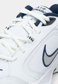 Sapatilha atlética branca com detalhes em azul marinho, apresentando um cabedal de couro liso, atacadores texturizados e um destacado logo da Nike em prata.