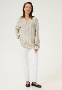 Beige skjorte med knapper og lodrette striber, lange ærmer og en afslappet pasform, parret med hvide lige bukser og sorte slip-on sko.