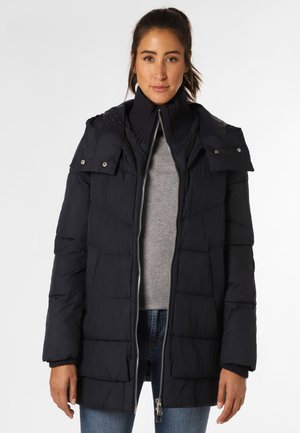 Navy puffer jacket with a high collar, quilted texture, front zipper, and snap-button details. Worn over a light gray sweater.