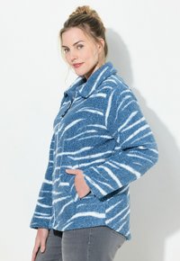 Niebieska i biała polarowa kurtka w paski z kołnierzem, długimi rękawami i dwoma bocznymi kieszeniami. Miękka tekstura i luźny krój.